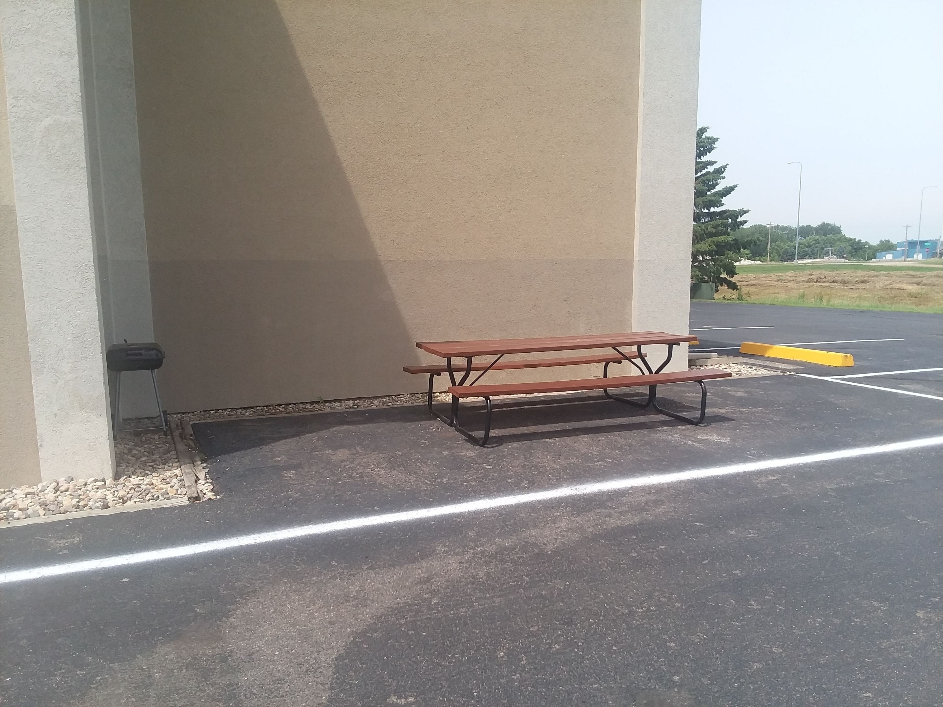 Une table de pique-nique se trouve sur un parking, avec un mur en béton et un champ d’herbe en arrière-plan.