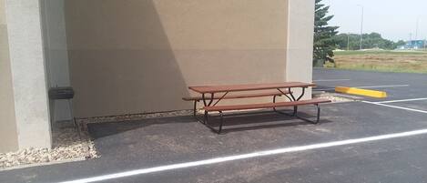 A picnic table in a parking lot with a concrete wall and a grassy field in the background.
