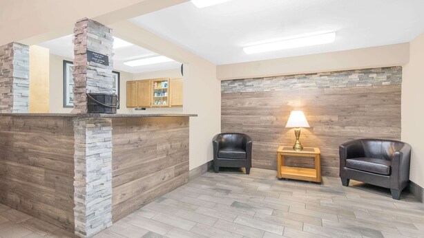 Zona de recepción con un pilar de piedra, pared de madera, dos sillones de cuero, una mesita con una lámpara y un mueble de madera.