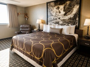Habitación de hotel con una cama grande, una silla, un escritorio, una lámpara, un teléfono y un cuadro de una cascada.