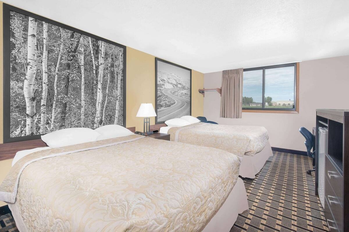 A hotel room with two beds, a desk, a lamp, a TV, and a window with a view.