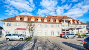 A hotel with a tiled roof, multiple windows, and a parking lot with several cars. - Leonardo Hotel Mannheim - Ladenburg (Ladenburg)