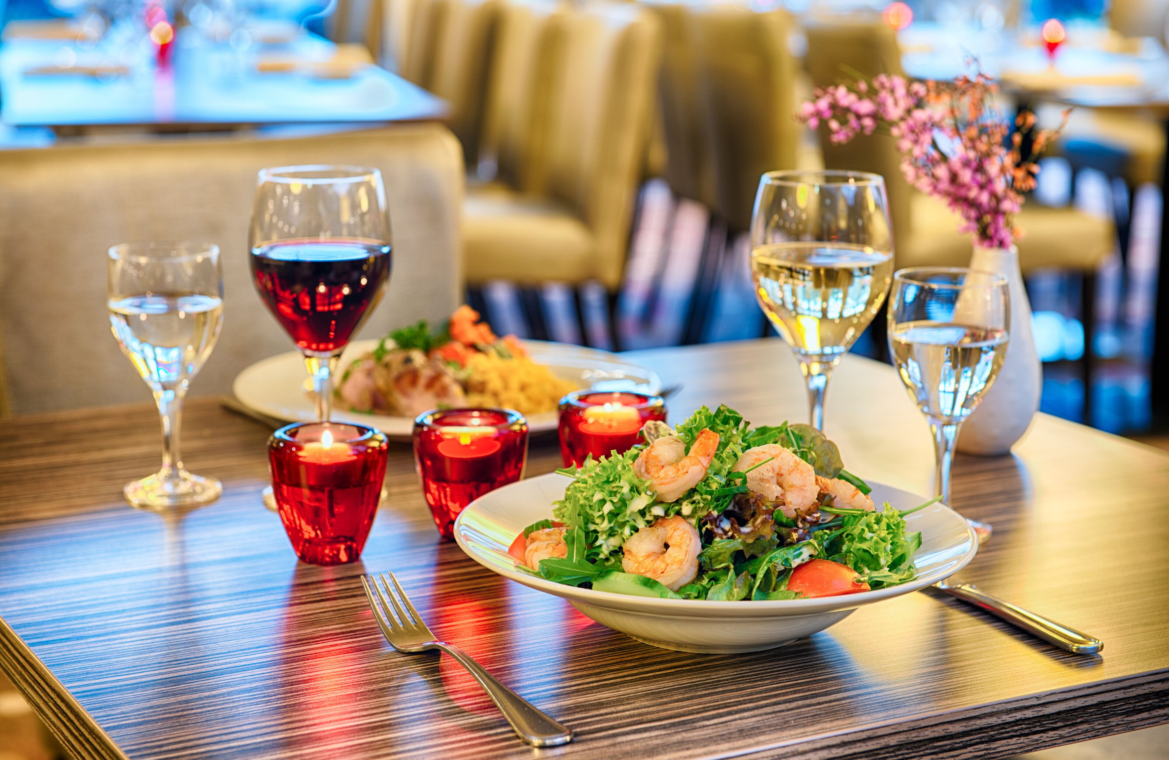 Een eettafel met garniturensalade, wijnglazen en kaarsen.