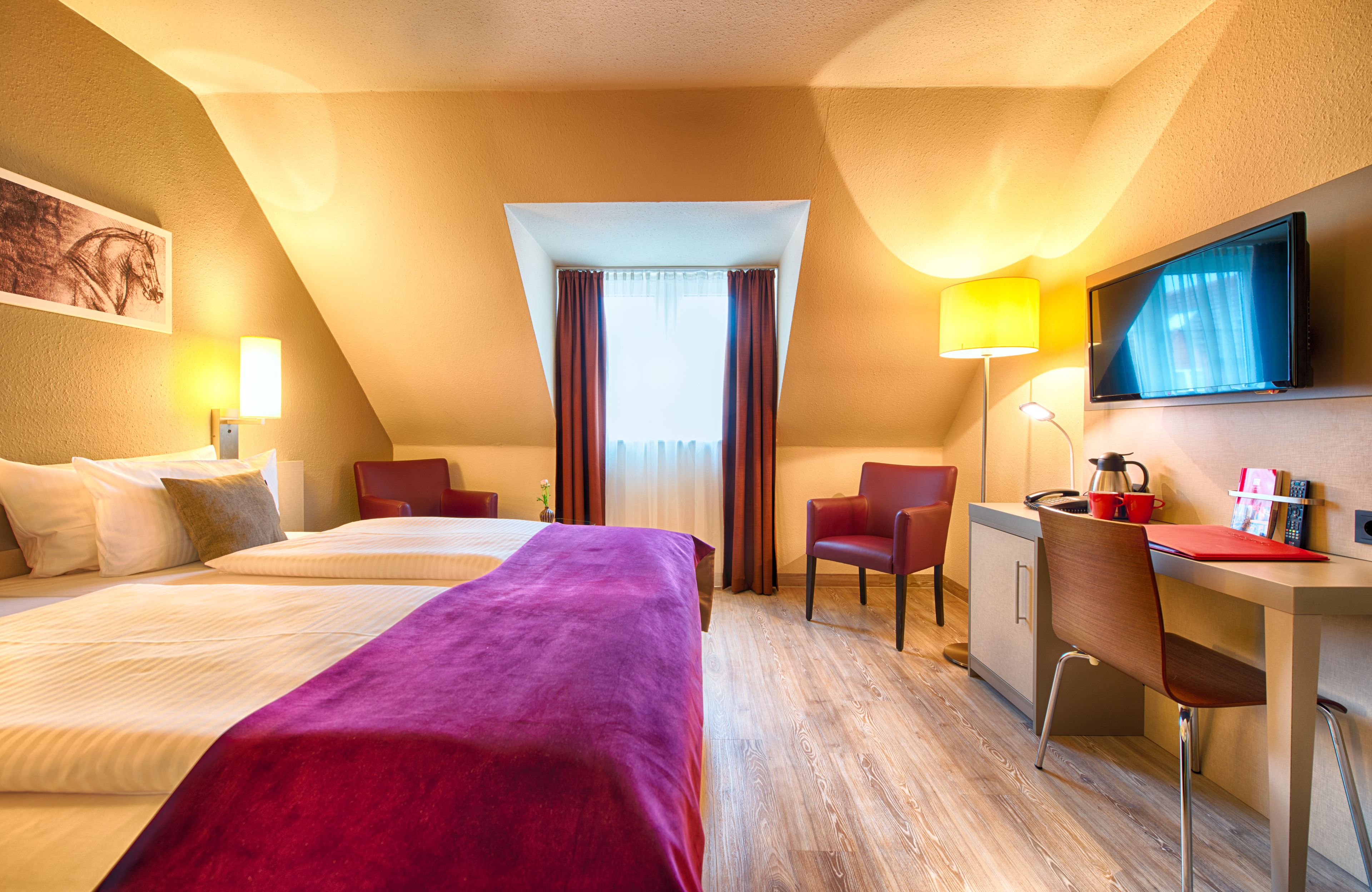 A hotel room with two beds, a desk, a chair, a television, and a window with curtains.