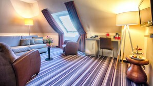 A hotel room with a sofa, armchair, dining table, and a small kitchenette. - Leonardo Hotel Mannheim - Ladenburg (Ladenburg)