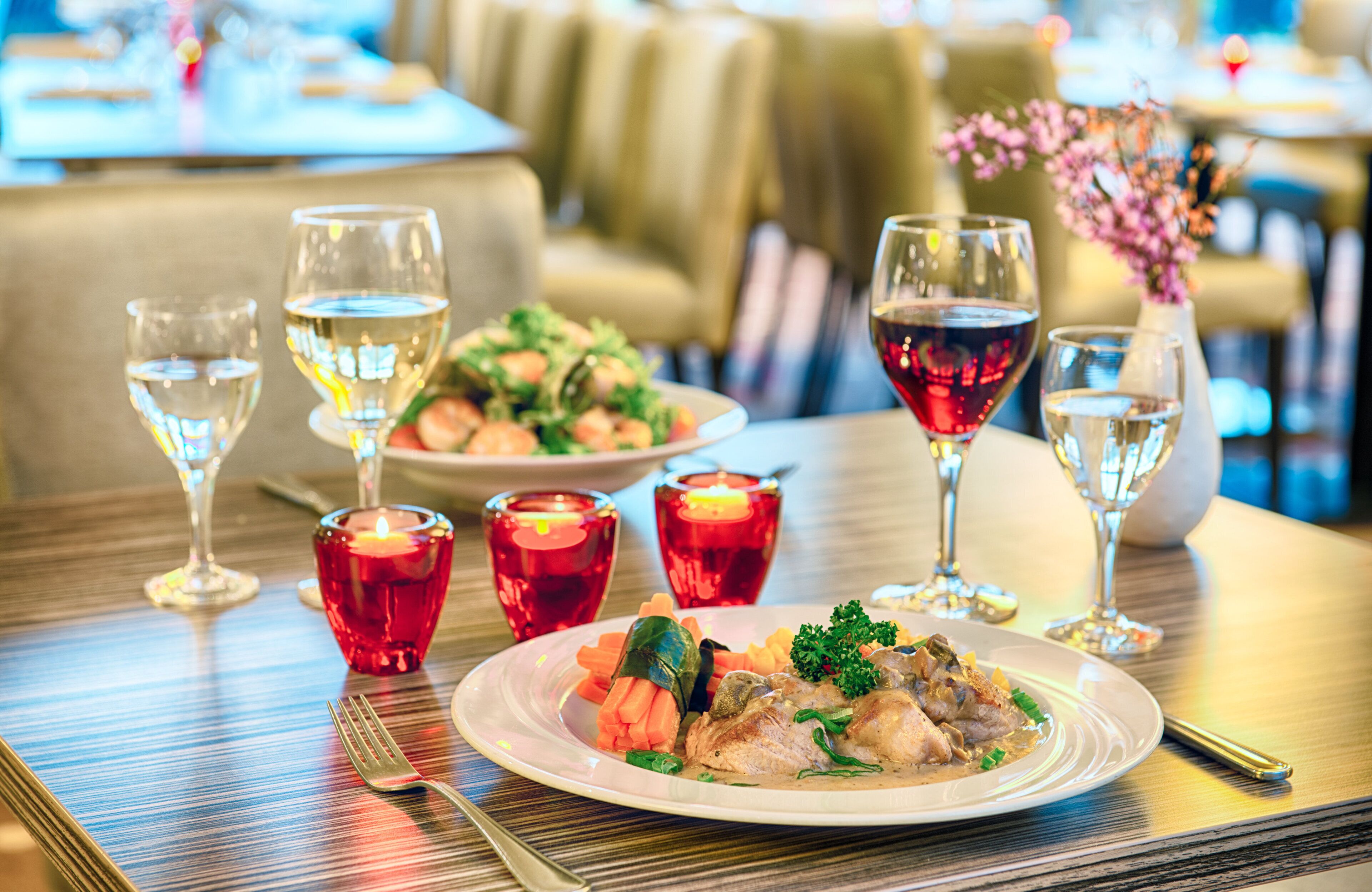 A dining table with a plate of food, glasses of wine, and candles.