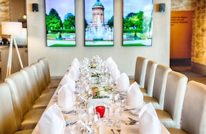 Una mesa de comedor dispuesta para una comida formal, con varias sillas, una vela roja y una pared con tres cuadros.
