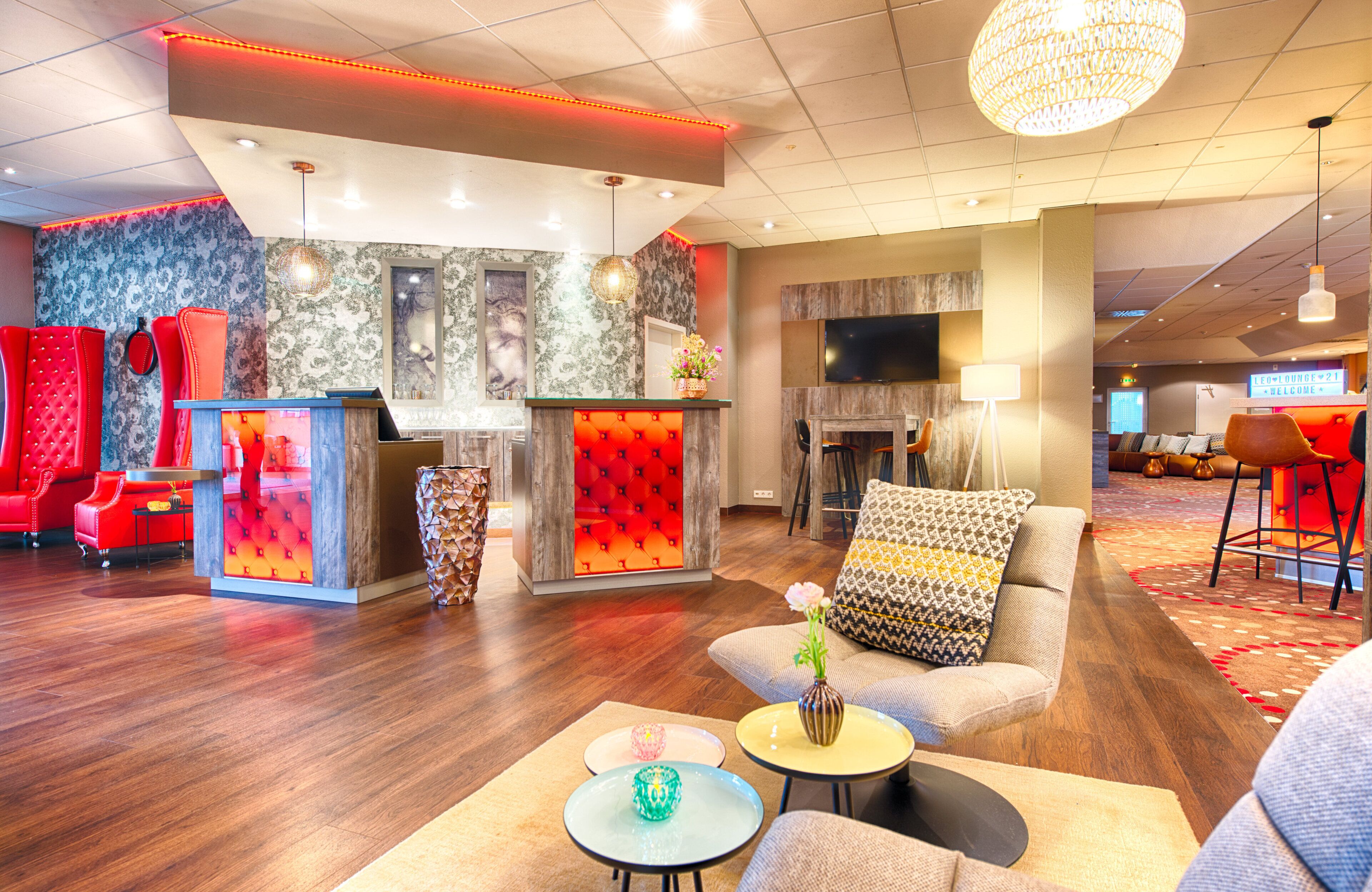 A hotel lobby with a reception desk, seating area, and a television screen.