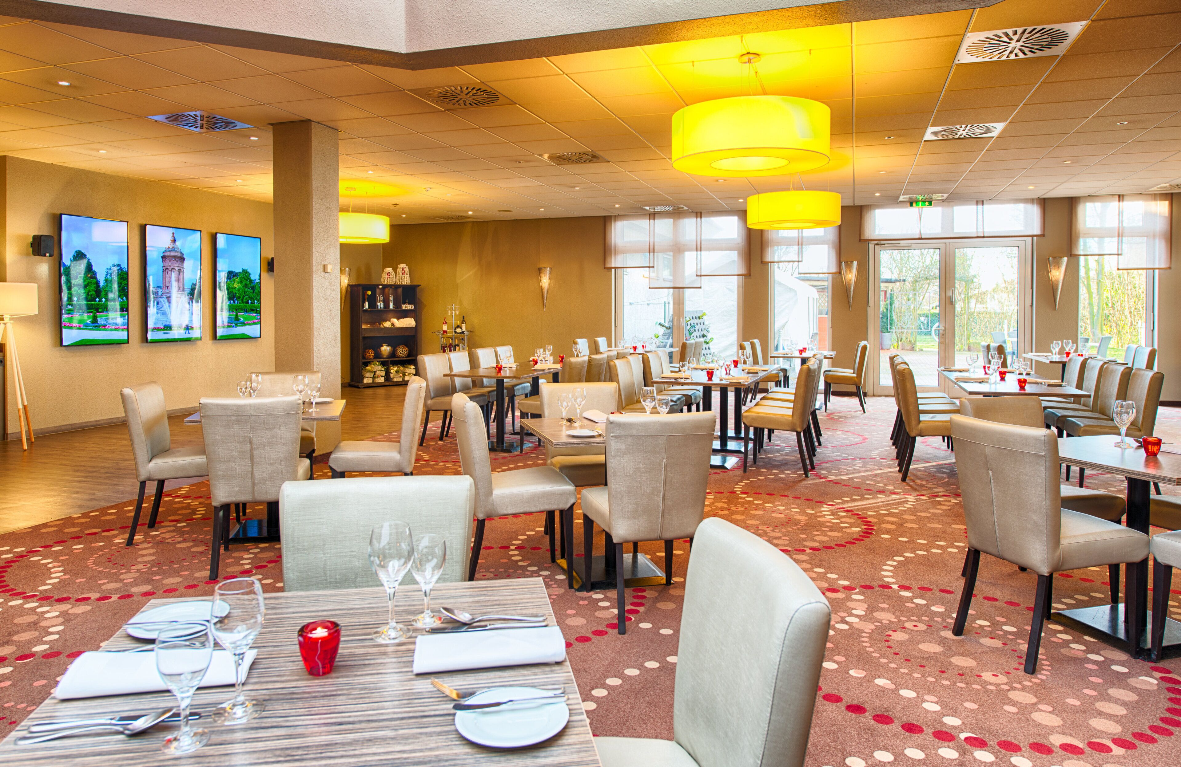 A hotel dining area with multiple tables and chairs, a chandelier, and artwork on the walls.