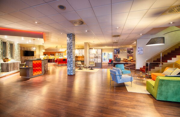 A spacious lobby with a wooden floor, a reception desk, seating area with chairs, and a staircase leading to upper floors. - Leonardo Hotel Mannheim - Ladenburg (Ladenburg)