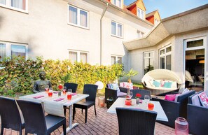 An outdoor patio area with wicker furniture, tables set for dining, and a statue of Buddha. - Leonardo Hotel Mannheim - Ladenburg (Ladenburg)