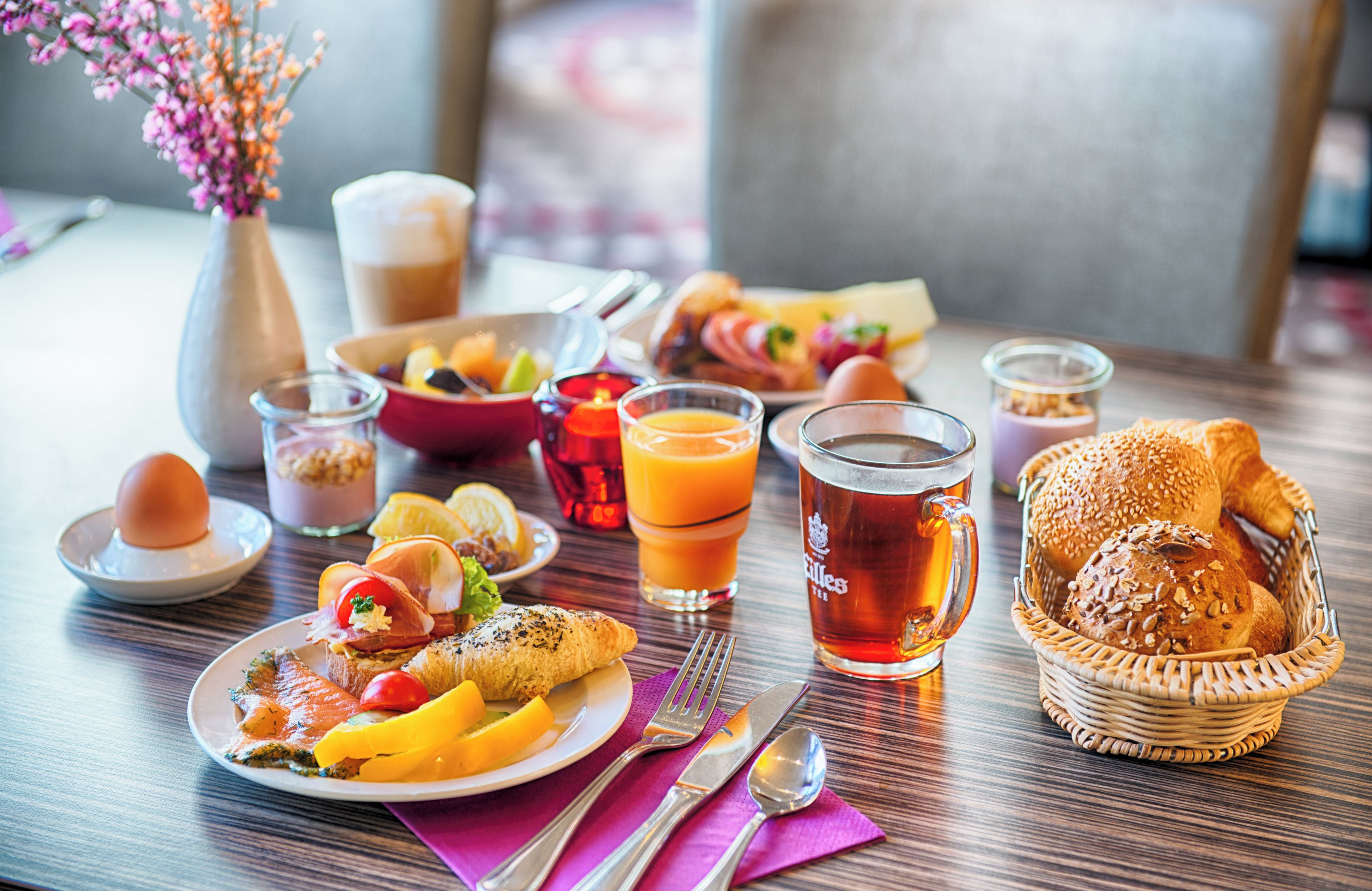 A breakfast setting with a variety of food items, drinks, and a basket of bread.