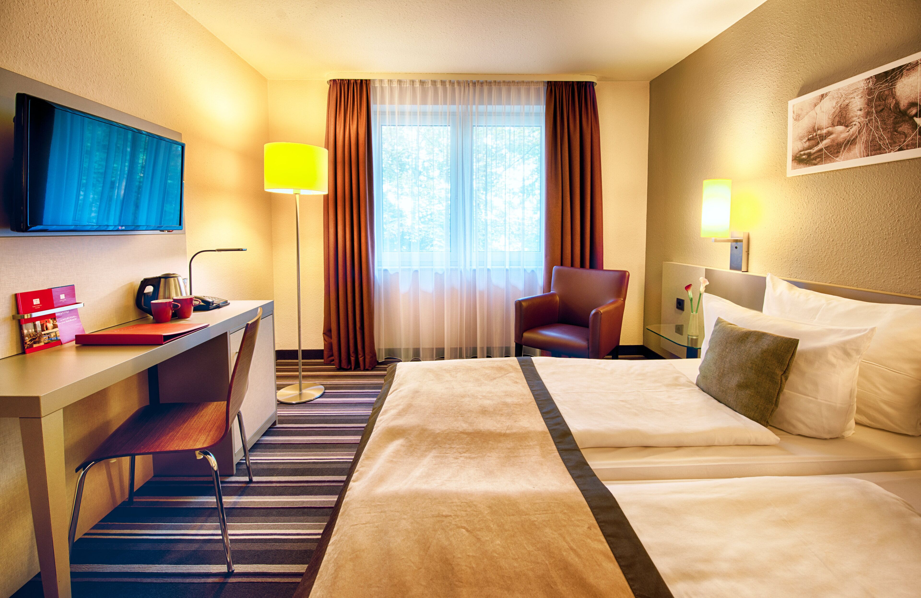 Hotelkamer met een bed, een bureau, een stoel, een televisie en een raam met gordijnen.