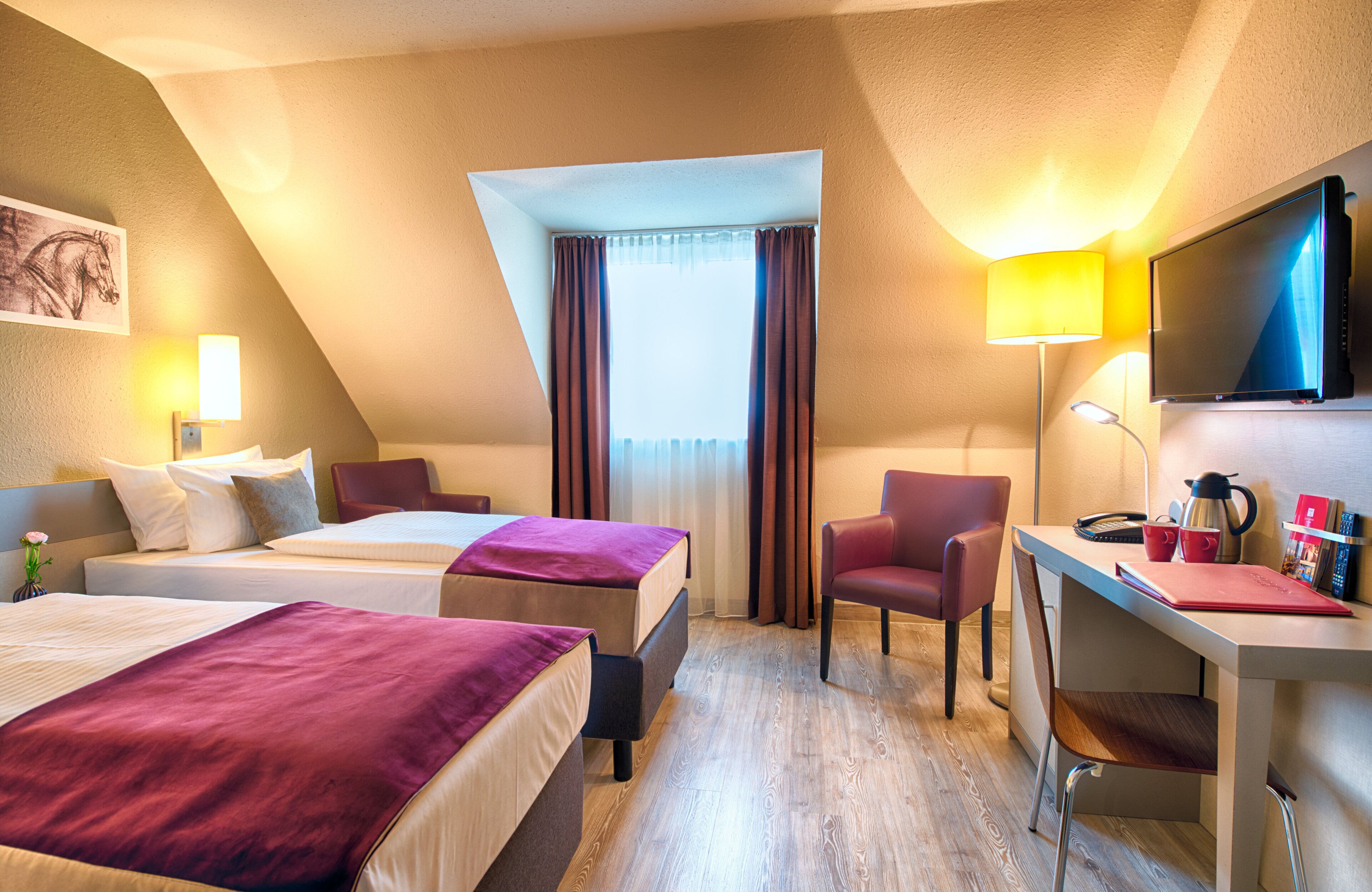 A hotel room with two beds, a desk, a chair, a TV, and a window with curtains.