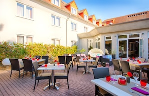 An outdoor dining area with tables and chairs, a Buddha statue, and a building with multiple windows and balconies. - Leonardo Hotel Mannheim - Ladenburg (Ladenburg)