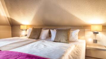 Habitación de hotel con techo alto, dos camas con sábanas blancas, varios almohadones y dos lámparas de noche.