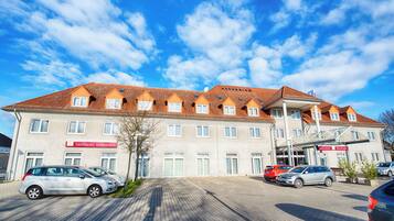Ein Hotel mit Ziegeldach, mehreren Fenstern und einem Parkplatz mit Autos.