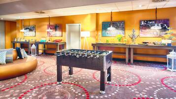 Una habitación con mesa de futbolín, sofá y mesa de buffet con comida y bebidas.