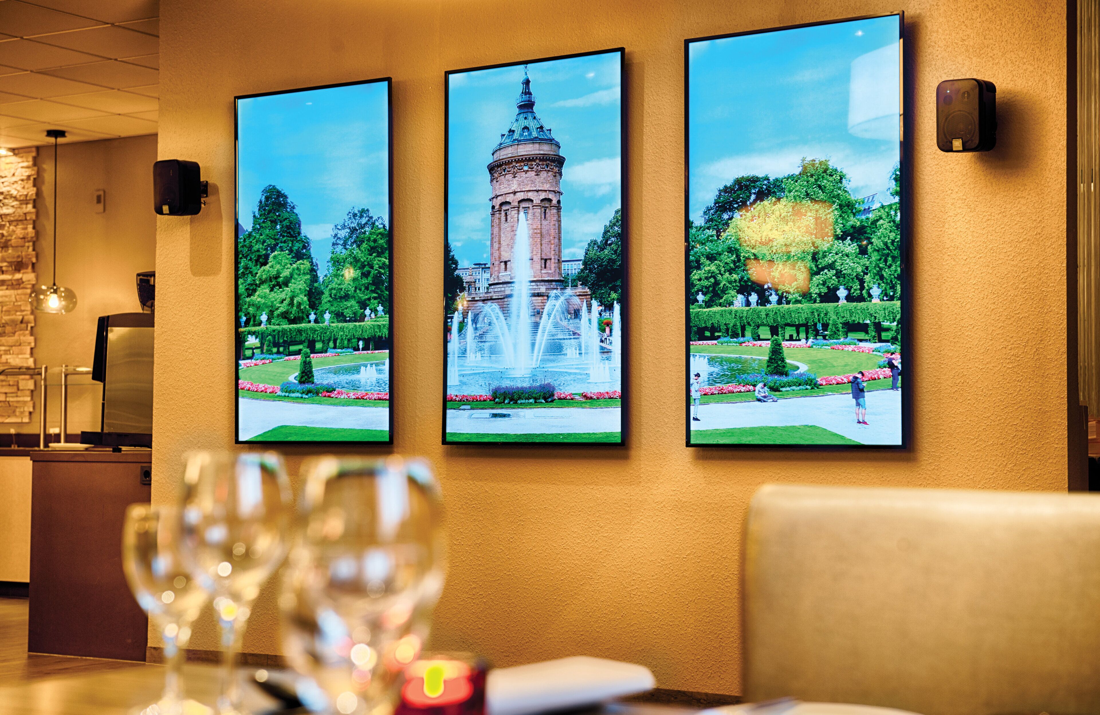 Un mur orné de trois tableaux encadrés représentant une tour et des jardins.