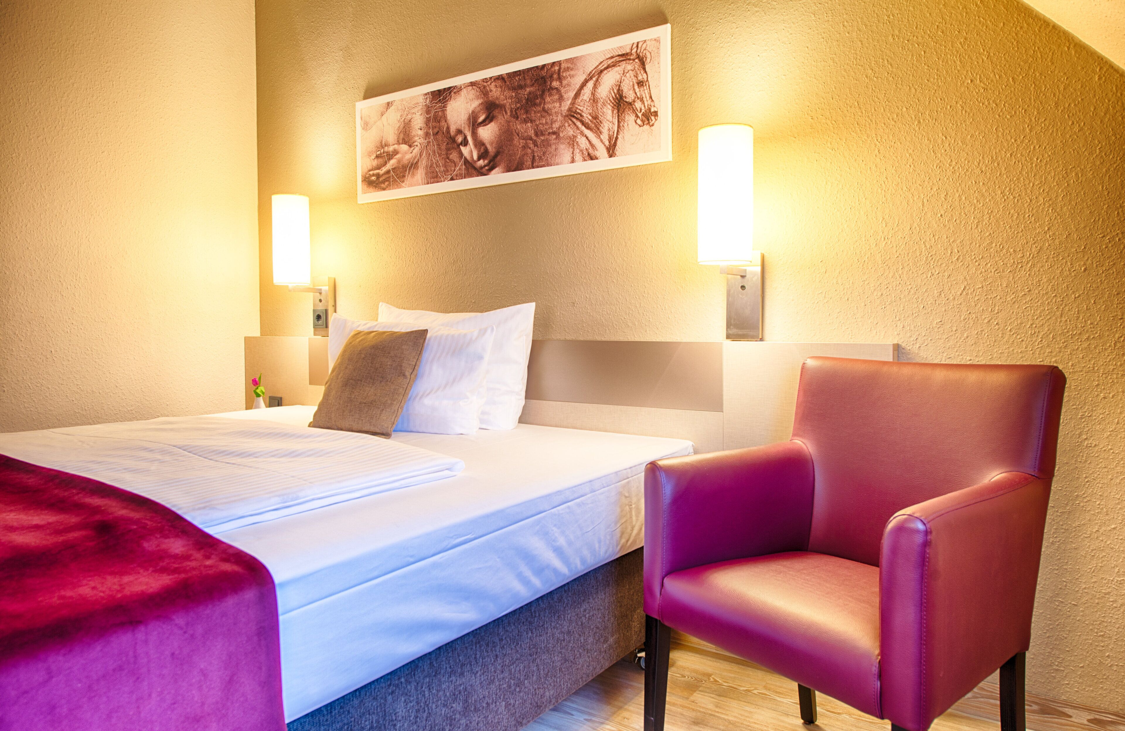 Una habitación de hotel con una cama, un sillón rojo y una obra de arte en la pared.