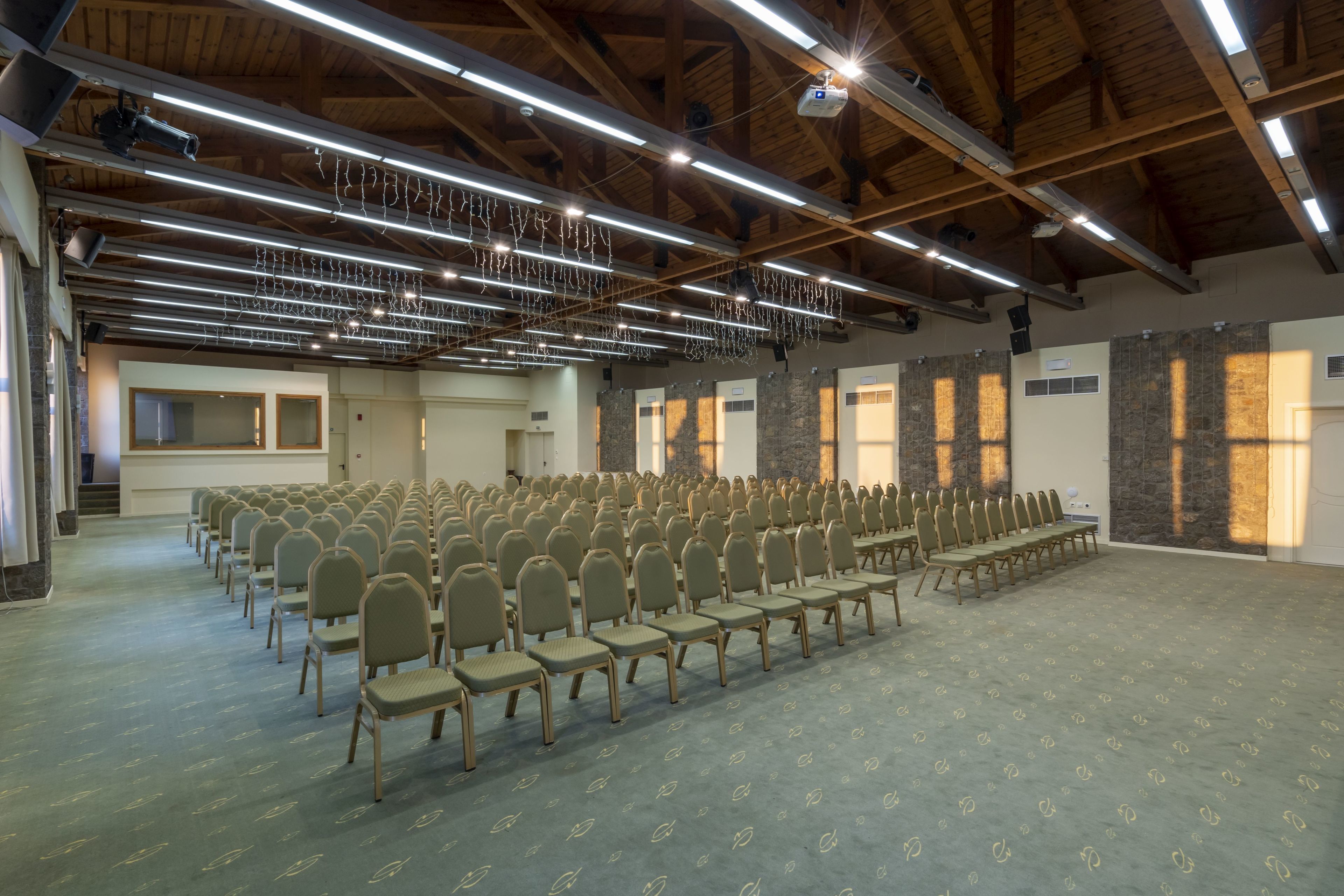 Un salón amplio con filas de sillas, vigas de madera y un techo alto con luminarias.