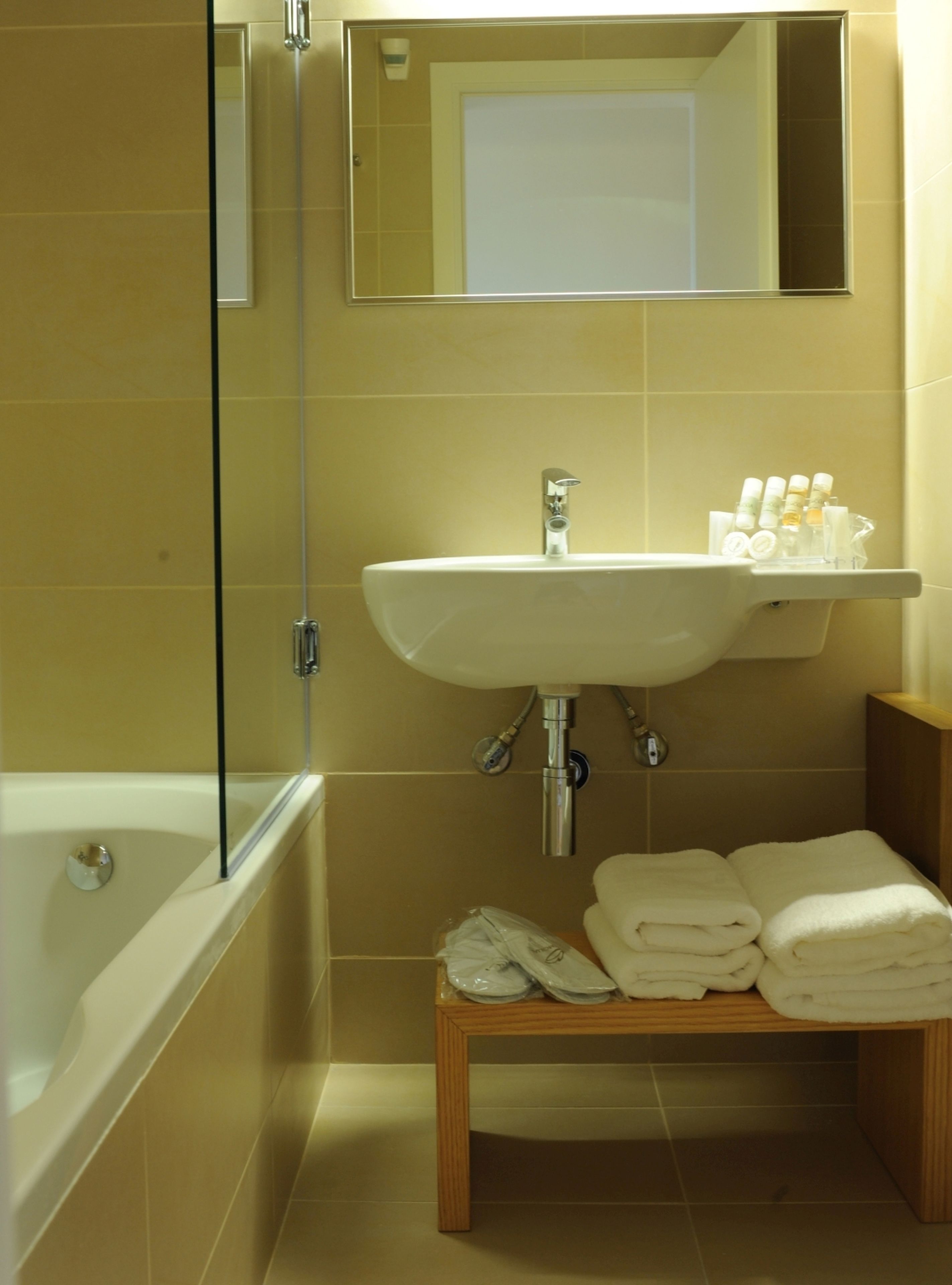 A bathroom with a bathtub, a sink, and a mirror. There are towels and toiletries on the sink.
