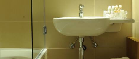 A bathroom with a bathtub, a sink, and a mirror. There are towels and toiletries on the sink.