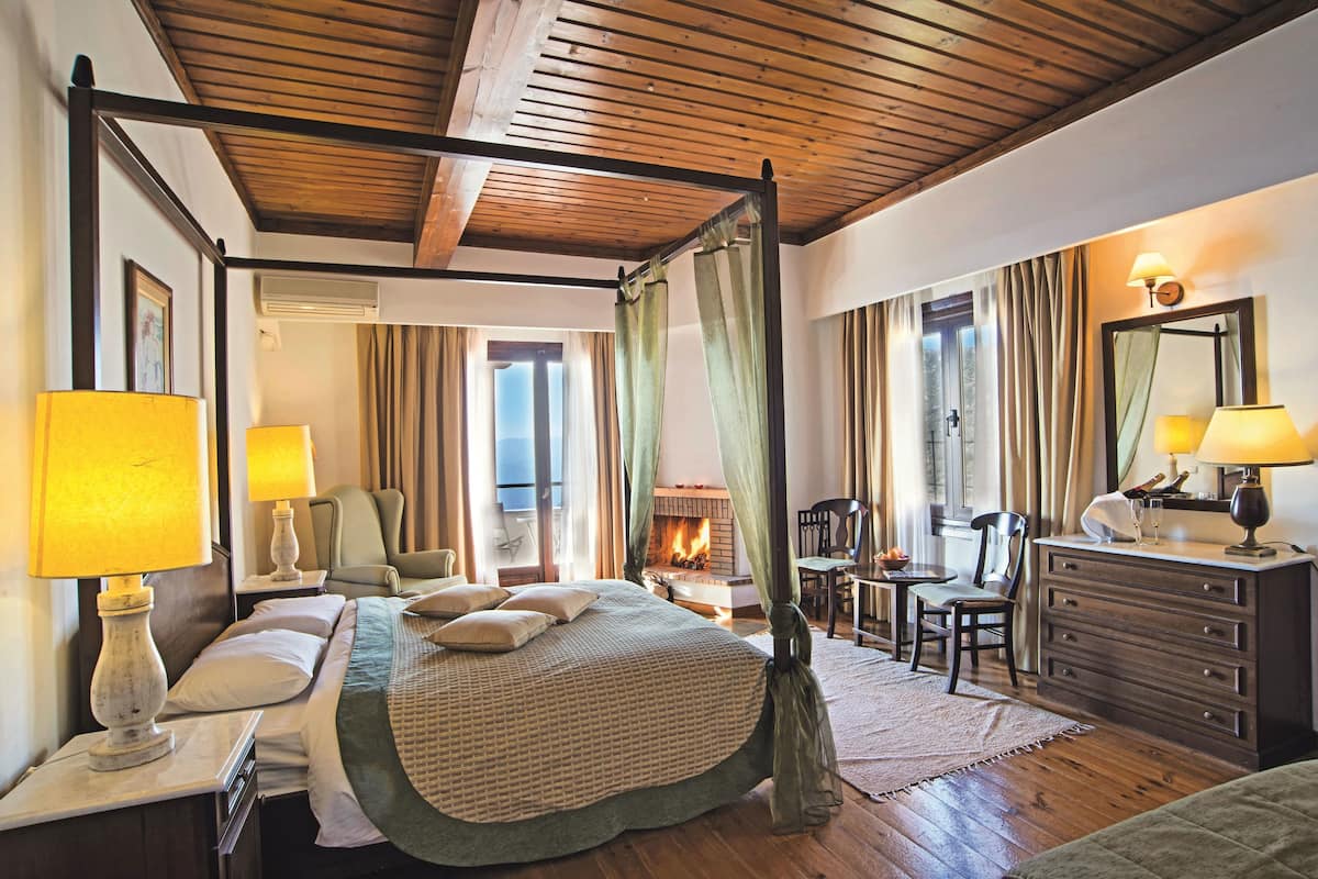 A bedroom with a four-poster bed, a wooden ceiling, a fireplace, and a desk with a chair.