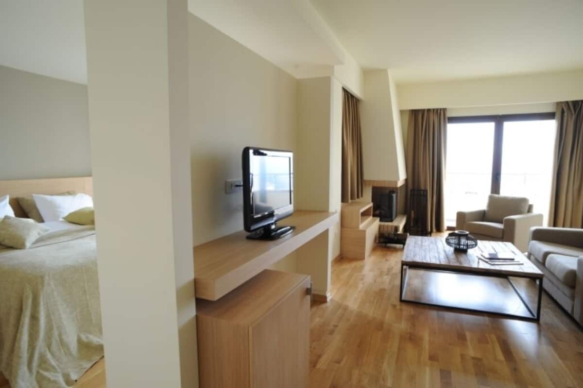 A hotel room with a bed, a TV on a wooden stand, a coffee table, and a sofa.