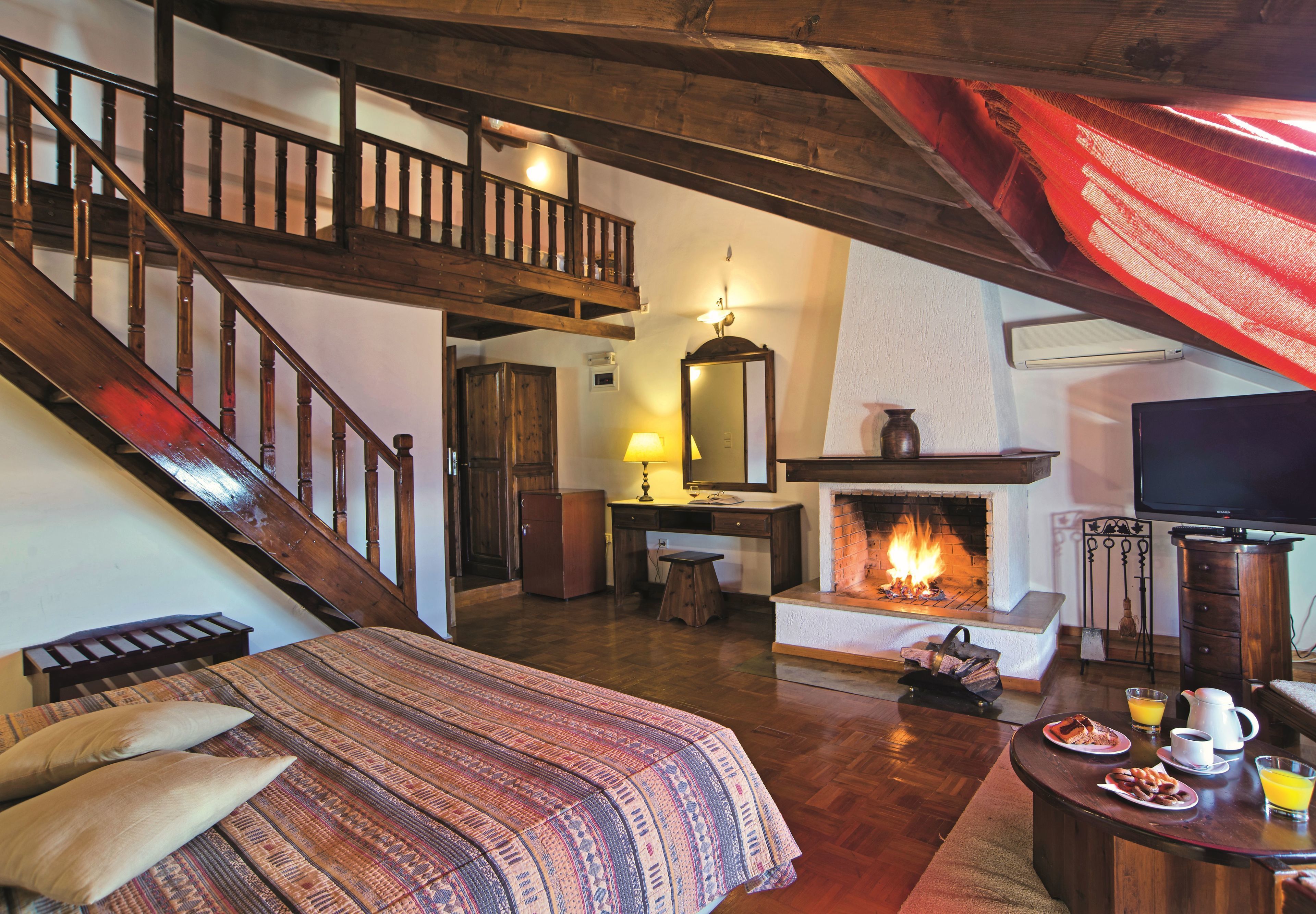 A cozy room with a bed, a fireplace, a television, and a dining area with breakfast items.