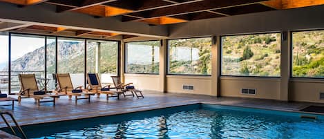 Un espace piscine doté de chaises longues et de grandes fenêtres offrant une vue sur un paysage montagneux.