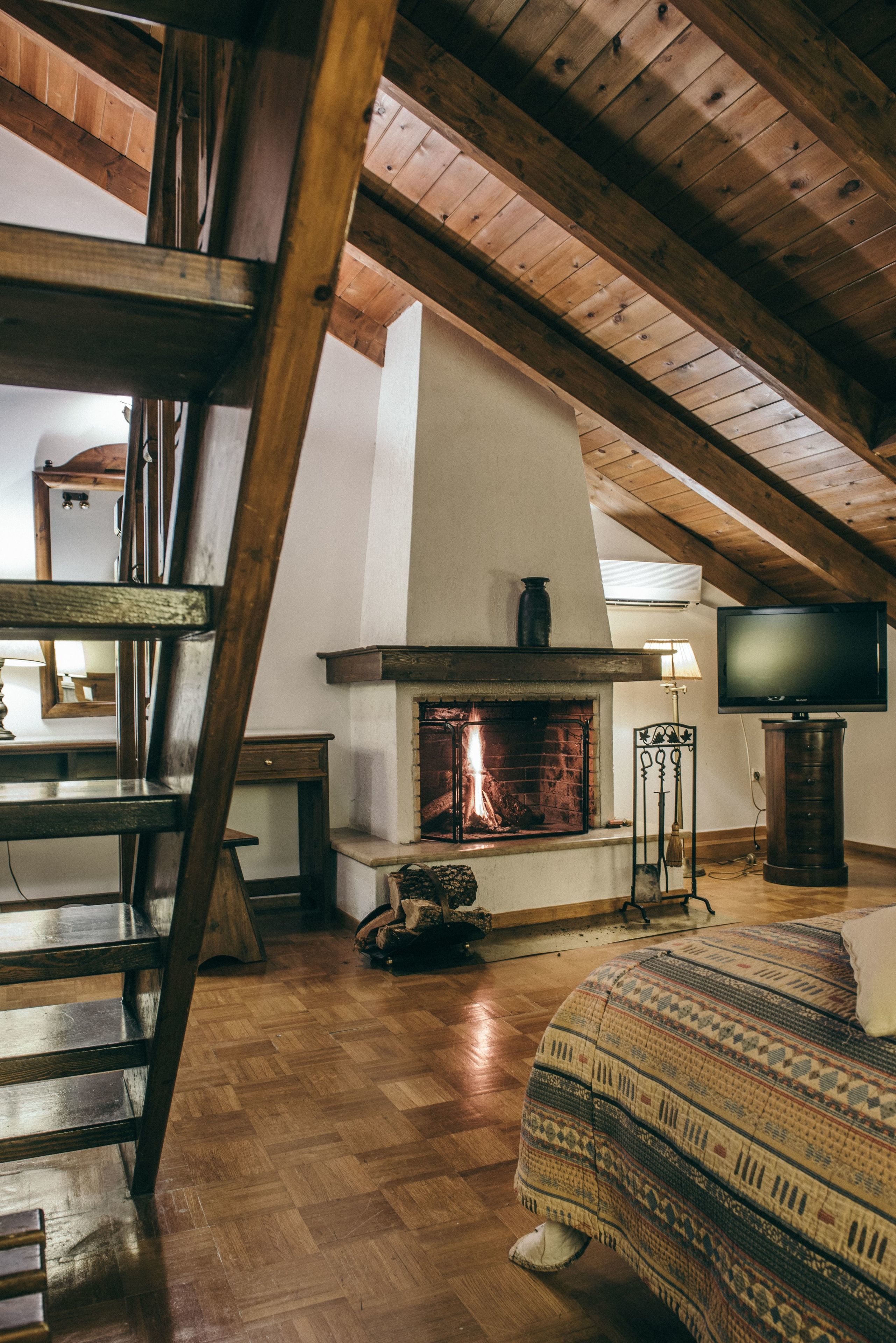 Una habitación acogedora con techo de madera, chimenea, televisor y cama con ropa de cama estampada.