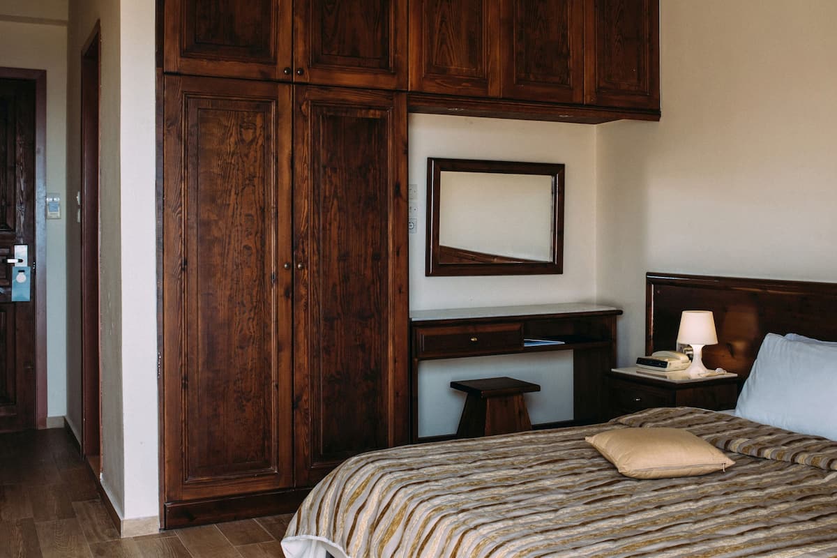 A bedroom with a large bed, a nightstand, a wooden wardrobe, and a mirror on the wall.