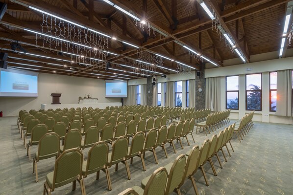 A conference room with rows of chairs, a projector screen, and large windows.