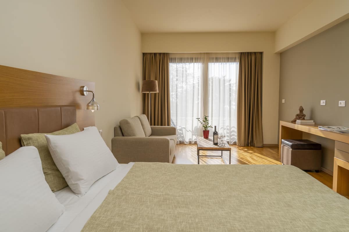 A hotel room with a bed, a sofa, a desk, and a window with curtains.