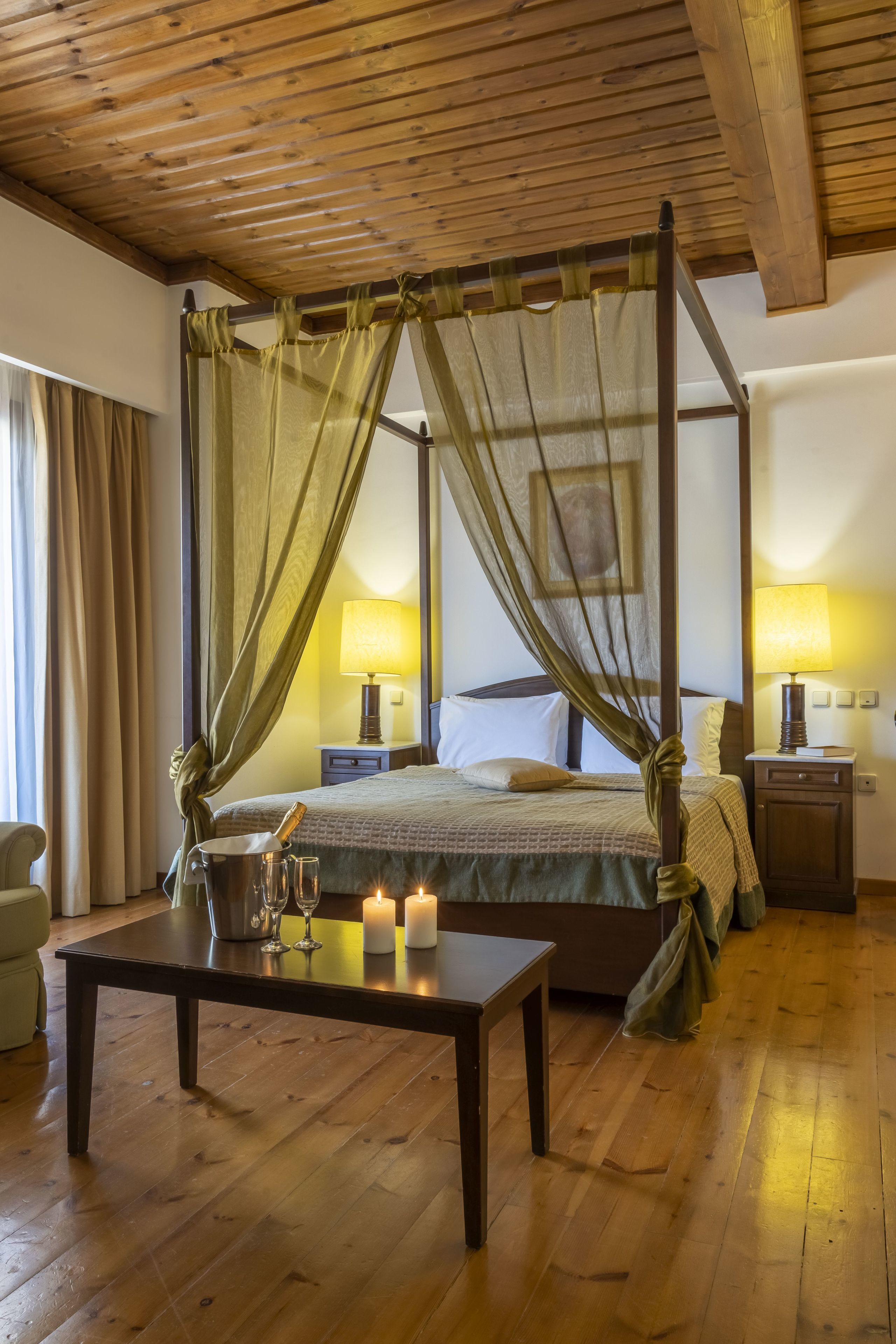 Una cama con dosel y cortinas, lámparas de noche, una mesita de noche con velas y suelo de madera.
