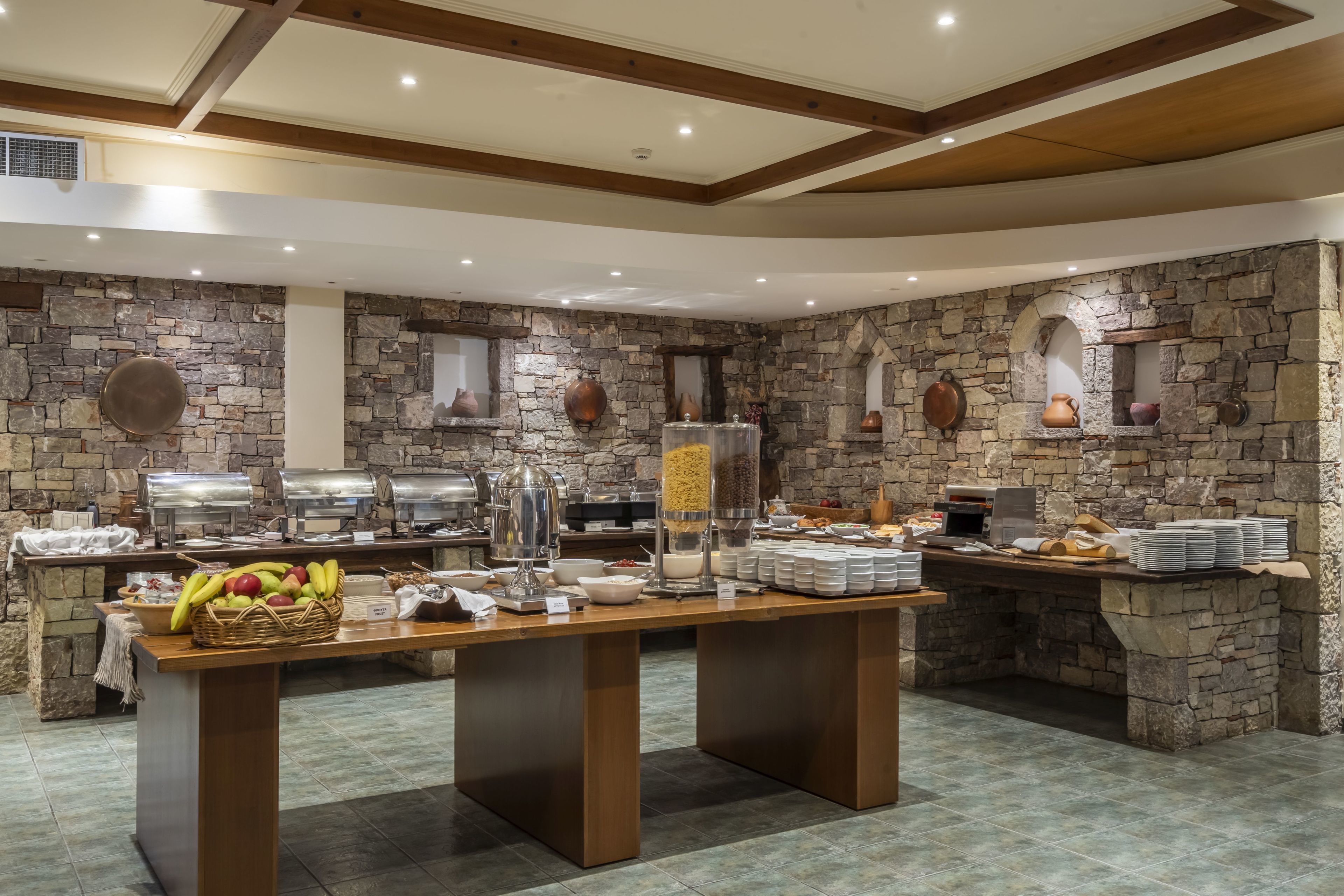 A buffet setup with stone walls, a wooden table, and various food and drink dispensers.