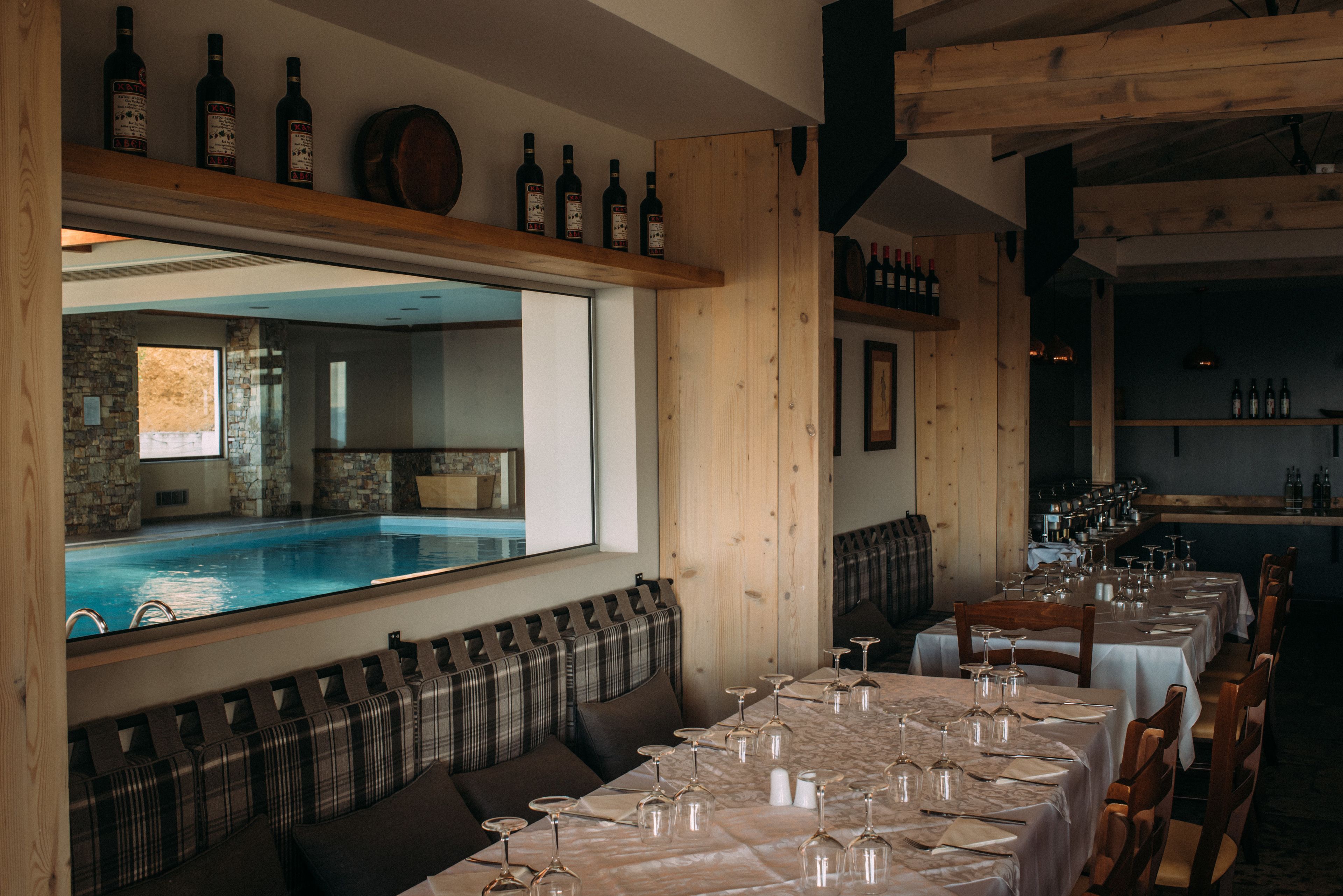 Een restaurant met uitzicht op een zwembad, houten meubels en wijnglazen op de tafels.