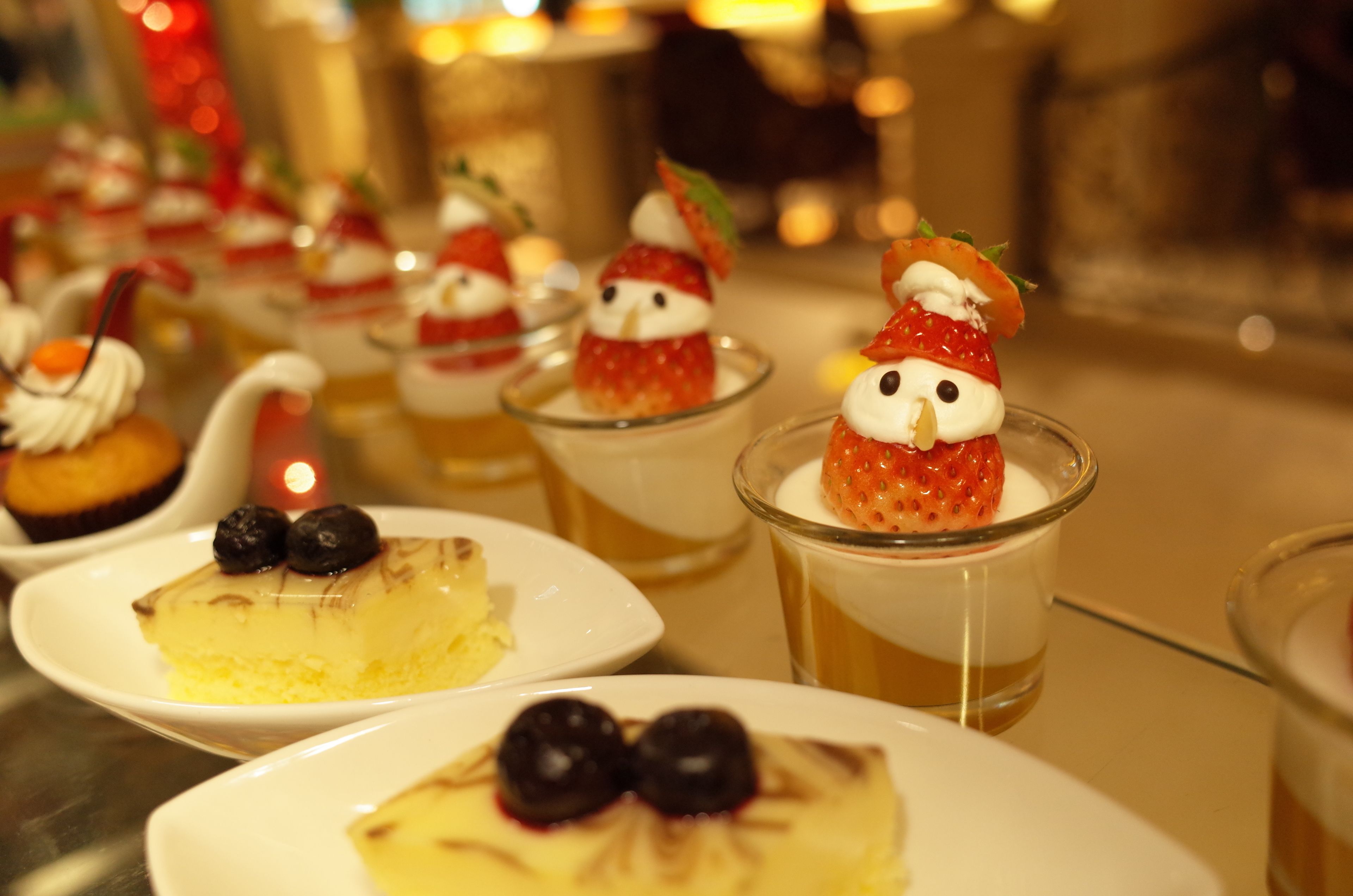Una mesa de postres con varios pequeños recipientes que contienen dulces, incluyendo un postre con fresas y un pastel de queso con arándanos.