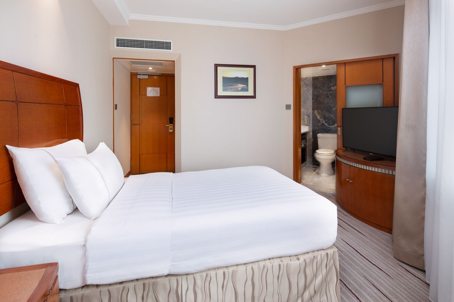 A hotel room with a large bed, a television, and a bathroom visible through an open door.