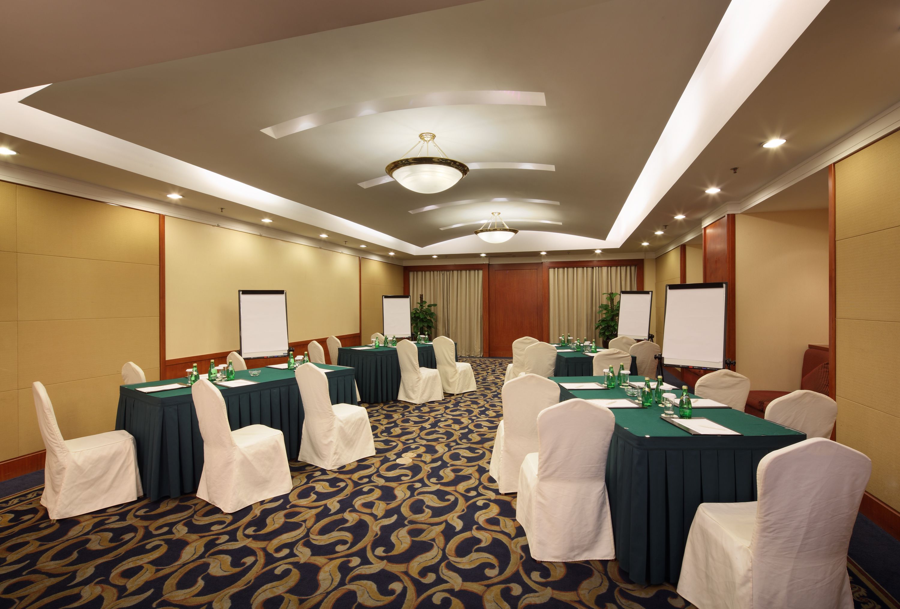A conference room with multiple tables, white chairs, and a carpeted floor.