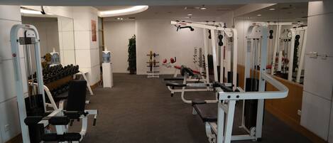 A gym with various exercise machines, a bench, and dumbbells.