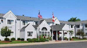 A row of white buildings with a central entrance, American flags, and a covered walkway. - CenterWay Hotel Buffalo North Near University (Tonawanda)