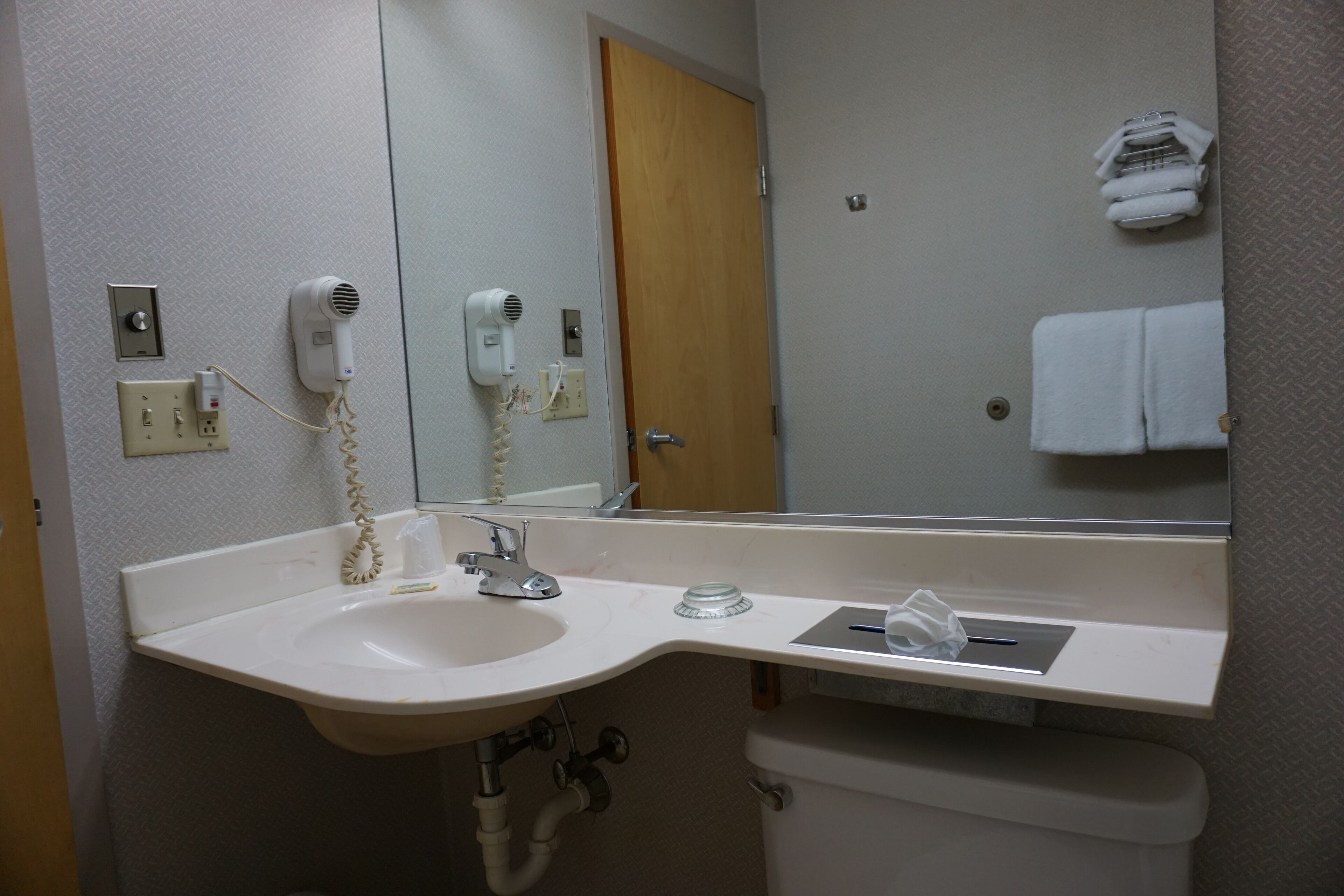 A bathroom with a sink, mirror, hairdryer, and towel rack.