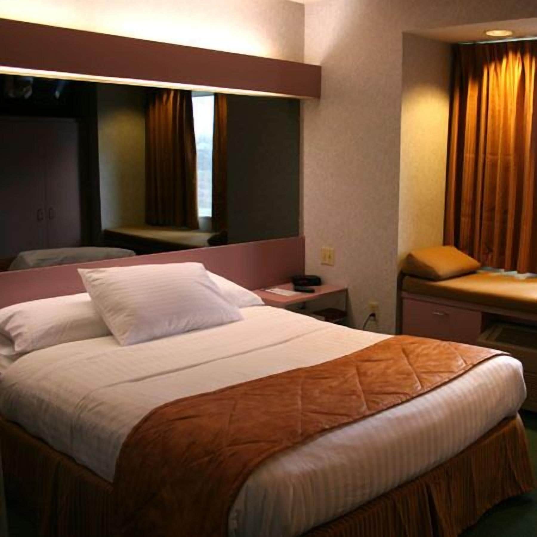 Une chambre d’hôtel avec un grand lit, une table de chevet, un miroir et une fenêtre avec des rideaux.