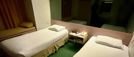 A hotel room with two single beds, a bedside table with a lamp, a mirror, and a green carpet.