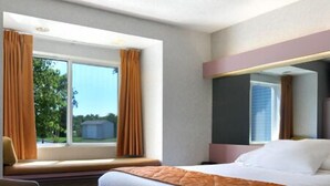 Ein Hotelzimmer mit einem großen Bett, einem Fenster mit Vorhängen, einem Sessel und Blick ins Freie.
