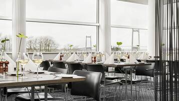 Un restaurante con varias mesas dispuestas para comer, ventanas amplias y vistas a un puente.