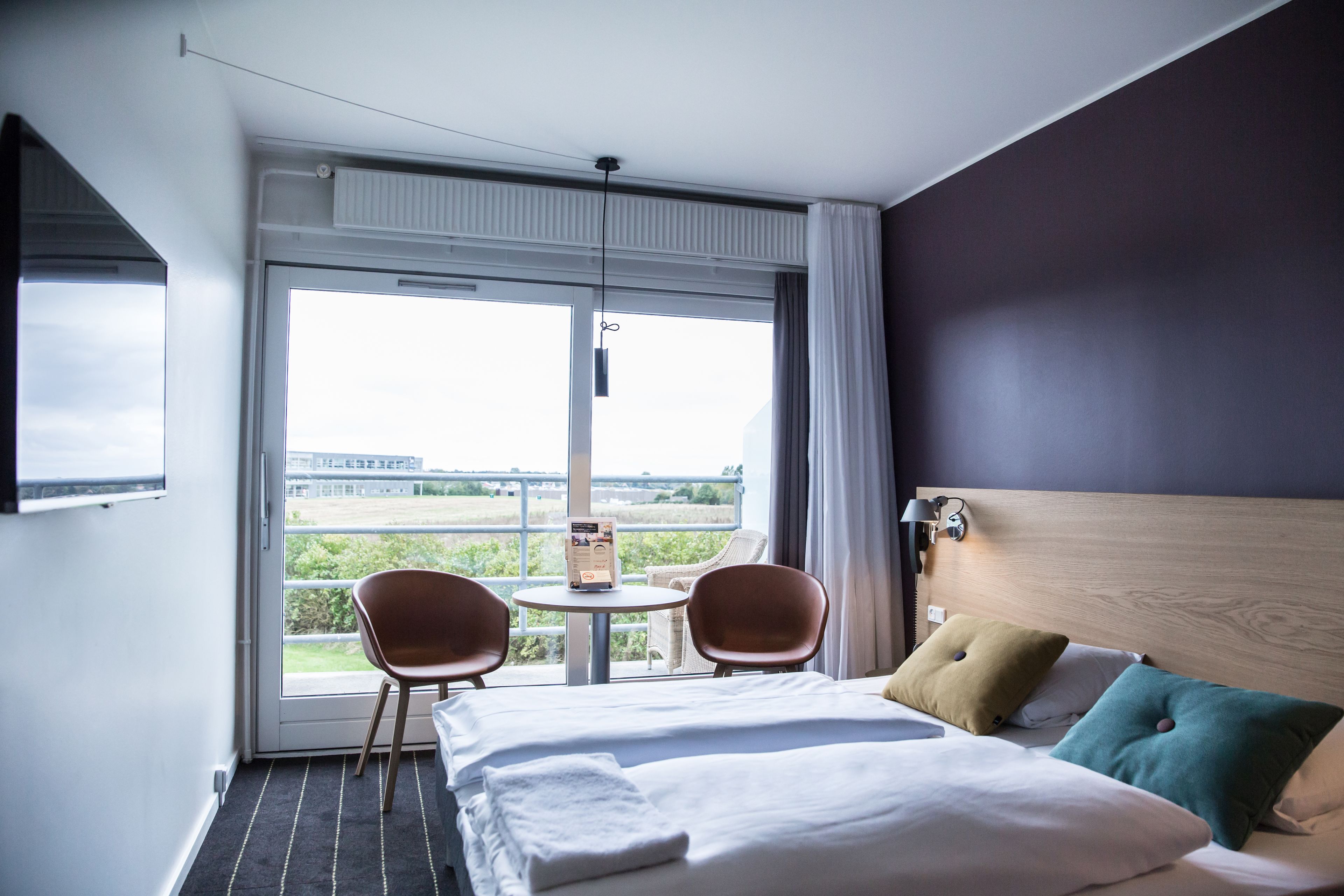 Habitación de hotel con cama, dos sillas, una mesita y vista al exterior.