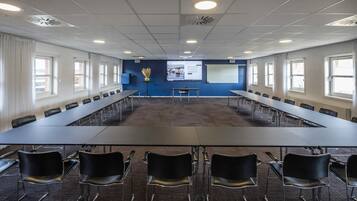 Een vergaderzaal met een lange tafel, stoelen, een projectiescherm en een presentatiescherm.